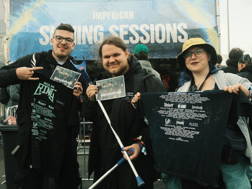 Drei Fans halten gerade signierte Autogrammkarten und T-Shirts in die Kamera