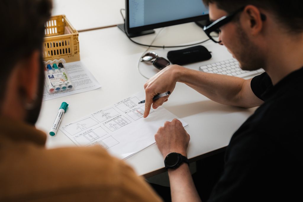 2 Leute, die auf einem Schreibtisch anhand eines aufgemalten Plans diskutieren